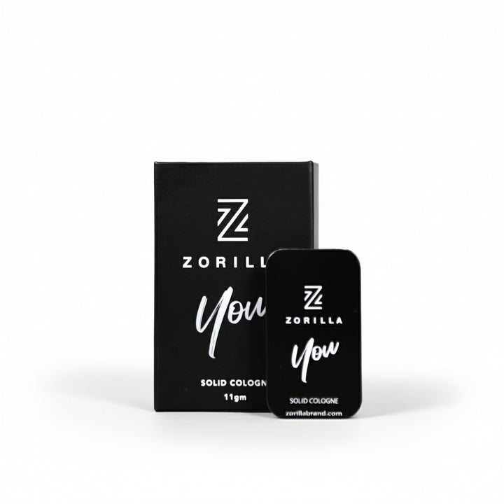 A small open black tin of Zorilla solid cologne with the brand name and product 'You' visible on the front. The product is presented in a slide-out box, suggesting a portable and easy-to-use design.